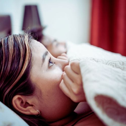 A woman lying in bed with the covers up around her face, looking scared - representing the Purple House Clinic's Psychosexual Therapy  Service.